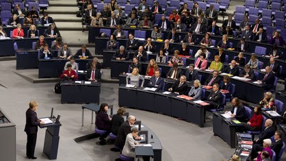 Eine Gruppe Politiker sitzt im Bundestag und hebt die Hände, während die Gruppe in der nächsten Sitzbank die Hände nicht hebt