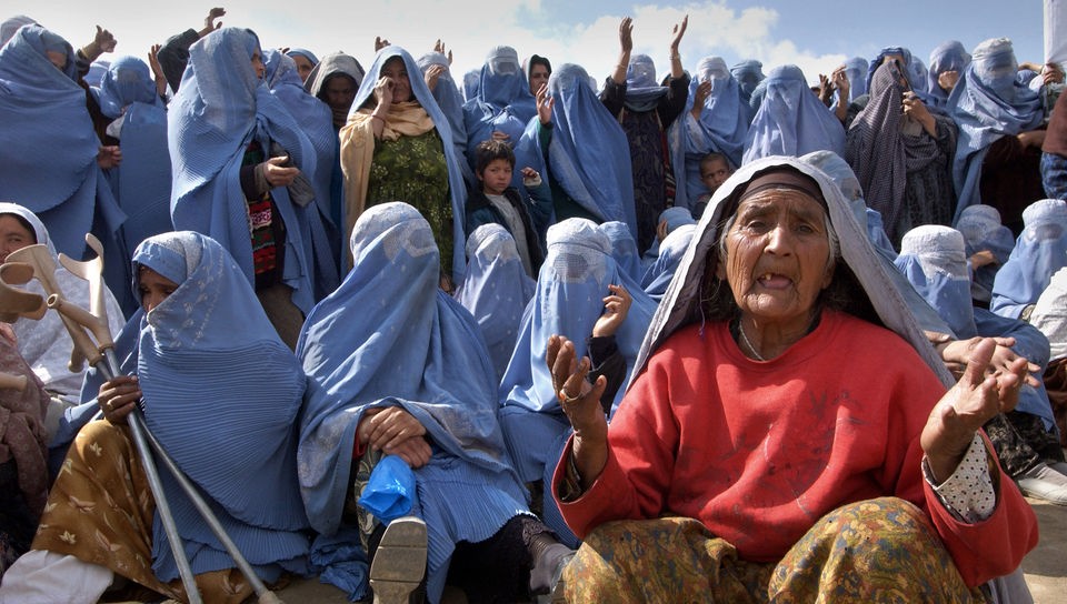 Afghanische Frau in einem blauen Gewand mit kleinem Jungen an der Hand geht über eine Straße