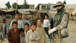 Deutscher Soldat steht neben einer Gruppe afghanischer Kinder und lächelt in die Kamera