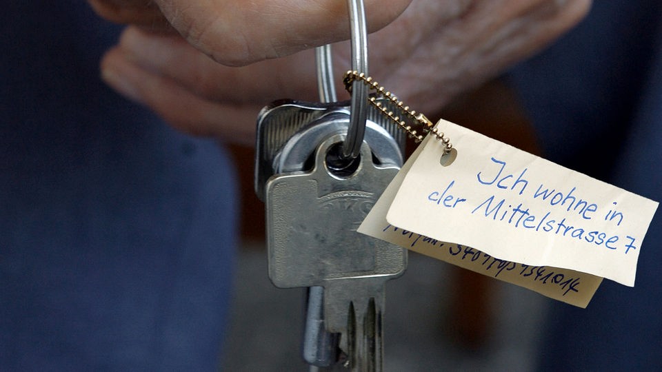 Hand hält Schlüsselbund mit Zettel, Aufschrift: Ich wohne in der Mittelstraße 7.