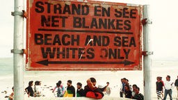 Schwarze stehen neben einem Schild, das einen Strandabschnitt für Weiße reserviert.
