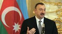 Präsident Ilham Alijew bei einer Rede vor der aserbaidschanischen Fahne.