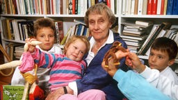 Astrid Lindgren in einem Sessel umringt von vier Kindern, von denen eines ein Buch in Händen hält