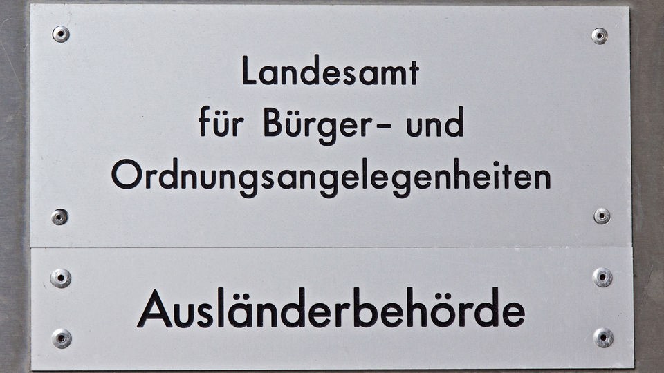 Schild 'Ausländerbehörde Berlin', dahinter undeutlich Menschen