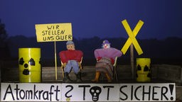 Drei Menschen stehen zwischen Artrappen von Atommüll-Behältern