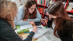 Drei Schülerinnen sitzen an Tisch und lernen gemeinsam.