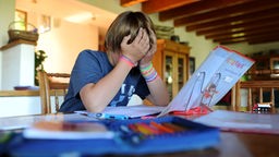 Ein zehnjähriger Junge hält beim Erledigen seiner Hausaufgaben seinen Kopf.