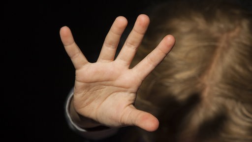 Ein Kind streckt seine Hand abwehrend in die Kamera.