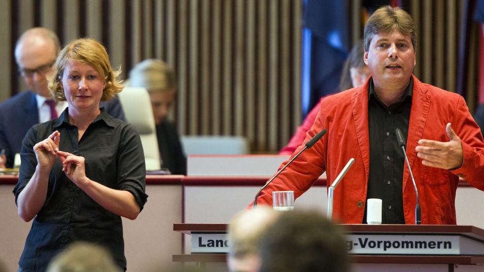 Eine Gebärdendolmetscherin steht neben einem Politiker und übersetzt in Gebärdensprache.