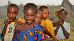 Afrikanisches Mädchen zwischen anderen Kindern lacht in Kamera.