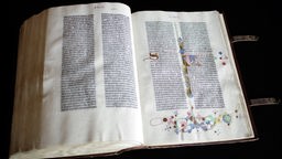 Eine Gutenberg-Bibel liegt aufgeschlagen auf schwarzem Stoff