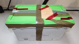 Weiße Box mit grünem Deckel ist mit Paketband umwickelt.