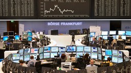 Mitarbeiter der Deutschen Börse sitzen vor ihren Computern, über ihnen die Anzeige der Aktienkurse