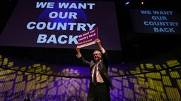 Der Politiker Nigel Farage hält ein Schild mit der Aufschrift ‚We Want Our Country Back‘.