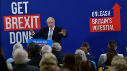 Boris Johnson bei einer Reder auf einer Tafel hinter ihm steht unter anderem'Get Brextit done!.