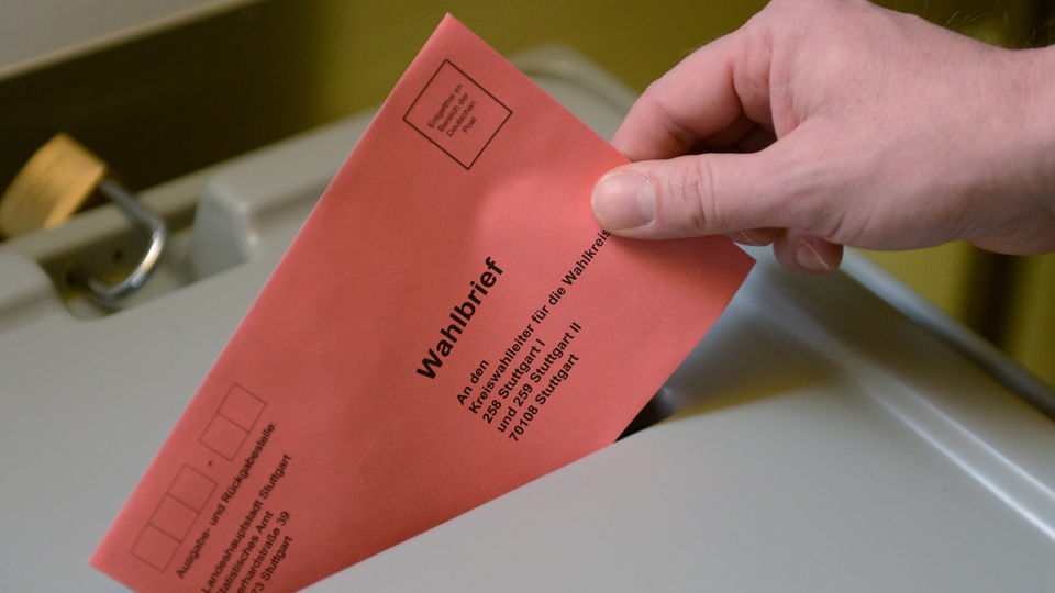 Hand hält Wahlbrief in den Schlitz einer Wahlurne