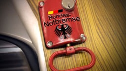 Notbremse in einem Zug mit kleiner Deutschland-Flagge und Aufschrift 'Bundes-Notbremse'.