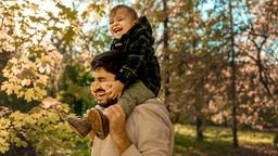 Lachender Vater trägt seinen Sohn im Park auf den Schultern. 