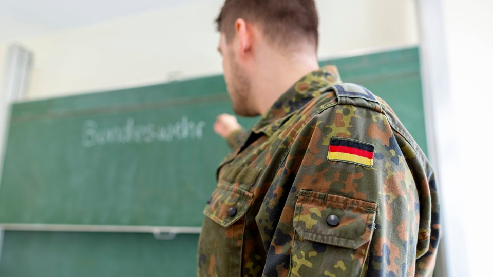 Soldat in Uniform steht vor Schultafel.