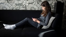 Ein Mädchen sitzt mit Handy in der Hand auf dem Sofa.