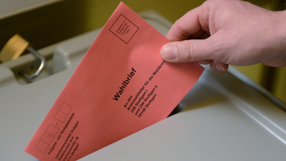 Hand steckt Wahlbrief in den Schlitz der Wahlurne