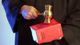 Hand hält deutsches Gesetzbuch, andere Hand schlägt mit Richterhammer darauf.
