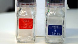 Zwei mit Plastik verschweißte leere Glasfläschchen, mit rotem und blauen Etikett und Schrift A-Probe, B-Probe.