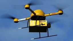 Eine Paket-Drohne der Deutschen Post fliegt mit einem Paket..
