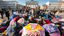 Zwei Demonstrantinnen sitzen vor dem Brandenburger Tor und halten ein Spruchband mit der Aufschrift &#8222;hiergeblieben&#8220;.