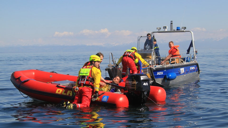 Helfer der DLRG und des Technischen Hilfswerks üben auf einem See die Bergung eines verletzten Person.