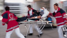 Drei Mitarbeiter des Deutschen Roten Kreuz schieben einen Patienten auf einer Liege vom Krankenwagen zum Krankenhauseingang