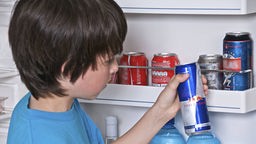 Ein Kind nimmt eine Dose Energydrink aus einem Kühlschrank, in dem auch Coladosen stehen.