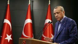 Recep Tayyip Erdoğan bei einer Rede neben drei Türkeifahnen.