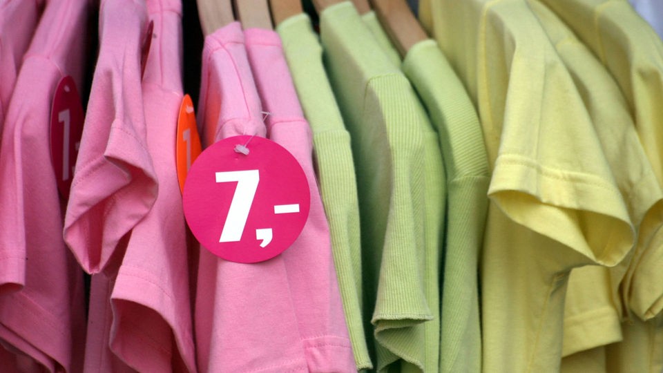 T-Shirts in verschiedenen Farben hängen auf einer Kleiderstange, davor Preisschild 7 Euro.