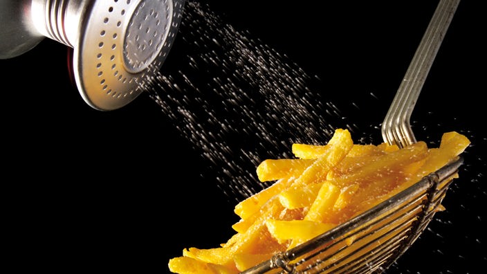Salz rieselt aus Salzstreuer auf Pommes Frites