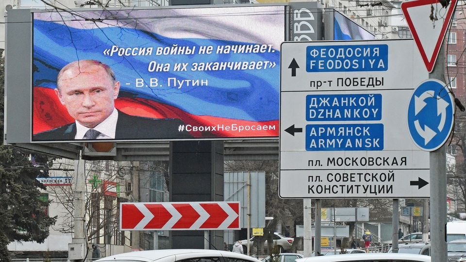 Display über einer Straße in Russland mit einem Portrait Wladimir Putins und einer russischen Aufschrift, die ins Deutsche übersetzt "Russland beginnt keine Kriege, es beendet sie" bedeutet.