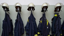 Helme und Uniformen von Feuerwehrleuten hängen sauber aufgereiht nebeneinander.