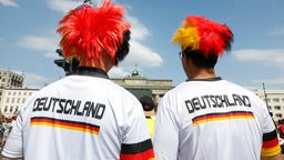 Zwei Fußballfans mit Deutschland-T'shirts und schwarz-rot-goldenen Perücken (von hinten).