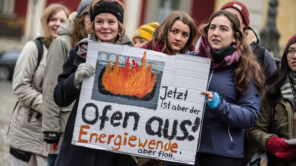 Schülerinnen halten Plakat mit Aufschrift 'Jetzt ist aber der Ofen aus! Energiewende, aber flott.'