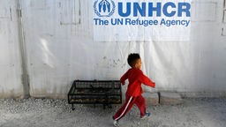 Ein kleiner Junge läuft in einem Flüchtlingslager an einem UNHCR-Logo vorbei. 