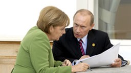 Merkel und Putin sitzen an einem Tisch und unterhalten sich