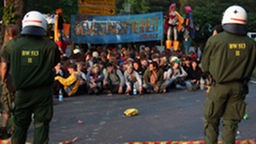 Demonstranten mit Plakat sitzen auf Straße, im Vordergrund zwei Polizisten.