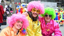 Drei junge Männer mit rosa Perücken und Shirts an Karneval.
