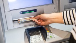 Eine Hand nimmt Scheine aus dem Schlitz an einem Geldautomaten.