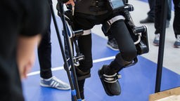 Beine stecken in Exoskelett, ein Bein wird hoch gehoben.
