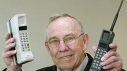 Der ehemalige Motorola Chefdesigner Rudy Krolopp hält zwei der ersten Mobiltelefone in den Händen.