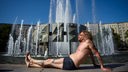 Mann in Badehose sonnt sich an einem Brunnen in der Stadt.