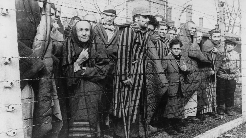 Eine Gruppe von Häftlingen steht hinter einem Zaun im Konzentrationslager Auschwitz