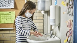 Schülerin mit Mund-Nasen-Schutz wäscht sich in Klasse die Hände.