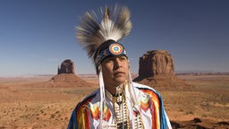 Ein Indianer steht in traditioneller Kleidung im Monument Valley Navajo Tribal Park in Arizona/USA.